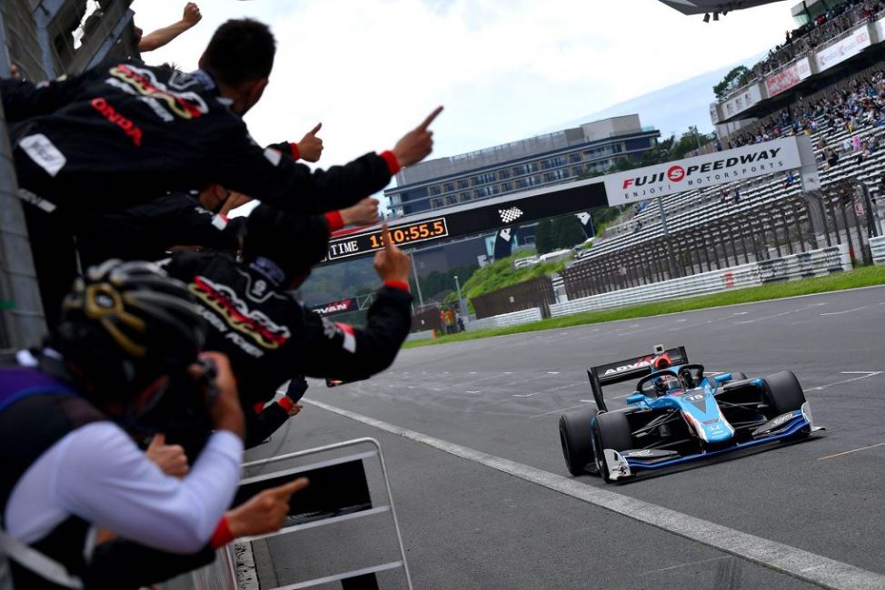 Blue Super Formula car crossing the line while people celebrate from the pit lane