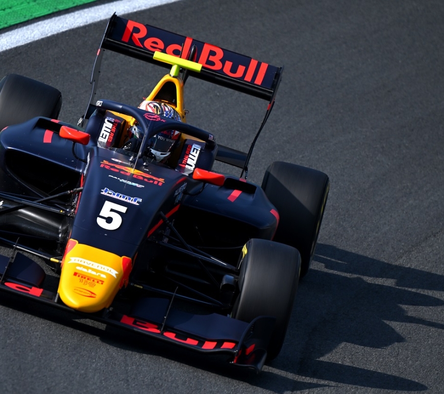 The blue, red and yellow Red Bull–sponsored Prema F3 car of Jak Crawford drives around the banking at the Turn 3 left-hander.