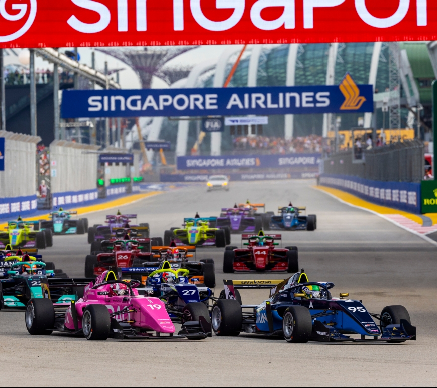 A grid of 18 cars prepares to make the left turn into Turn 1 at Singapore's Marina Bay Circuit on an overcast afternoon