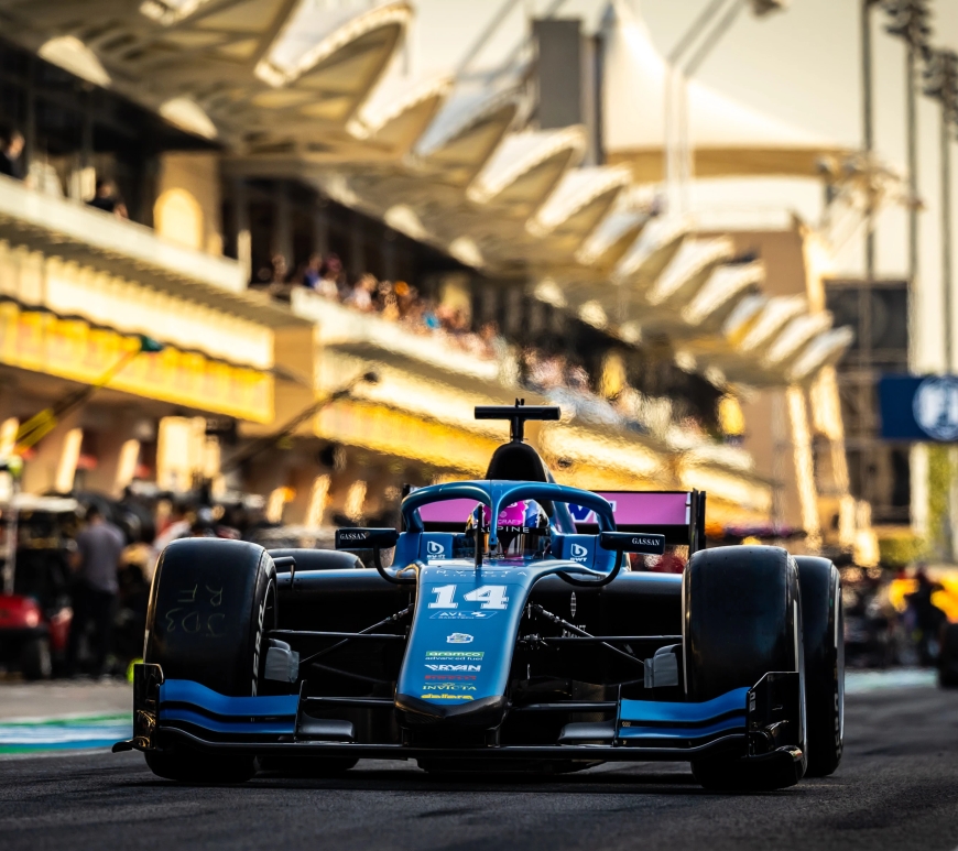 A blue and pink car on a yellow-hued, hazy pit lane, with a red car in the background