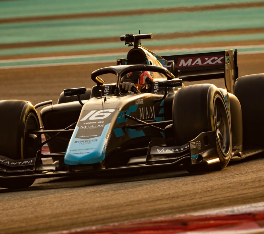 A navy and teal F2 car makes a right turn under fading light