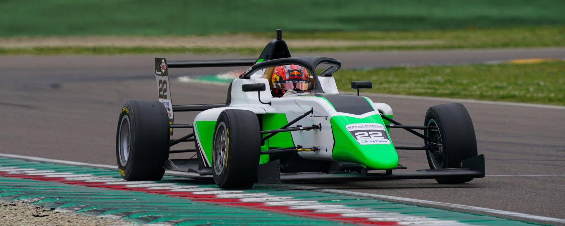 A green, white and black car with its right-side wheels against the rumble strips adorned with the Italian tricolore