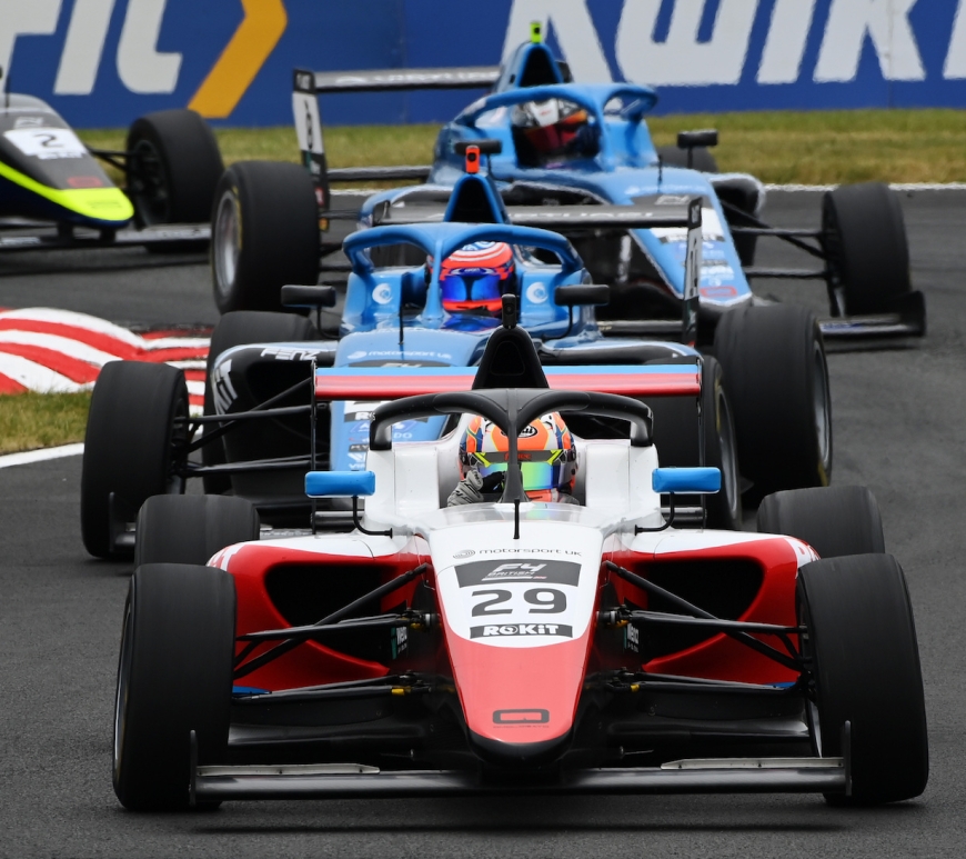 A red and white car followed by two blue cars and a green and black car going through the chicane