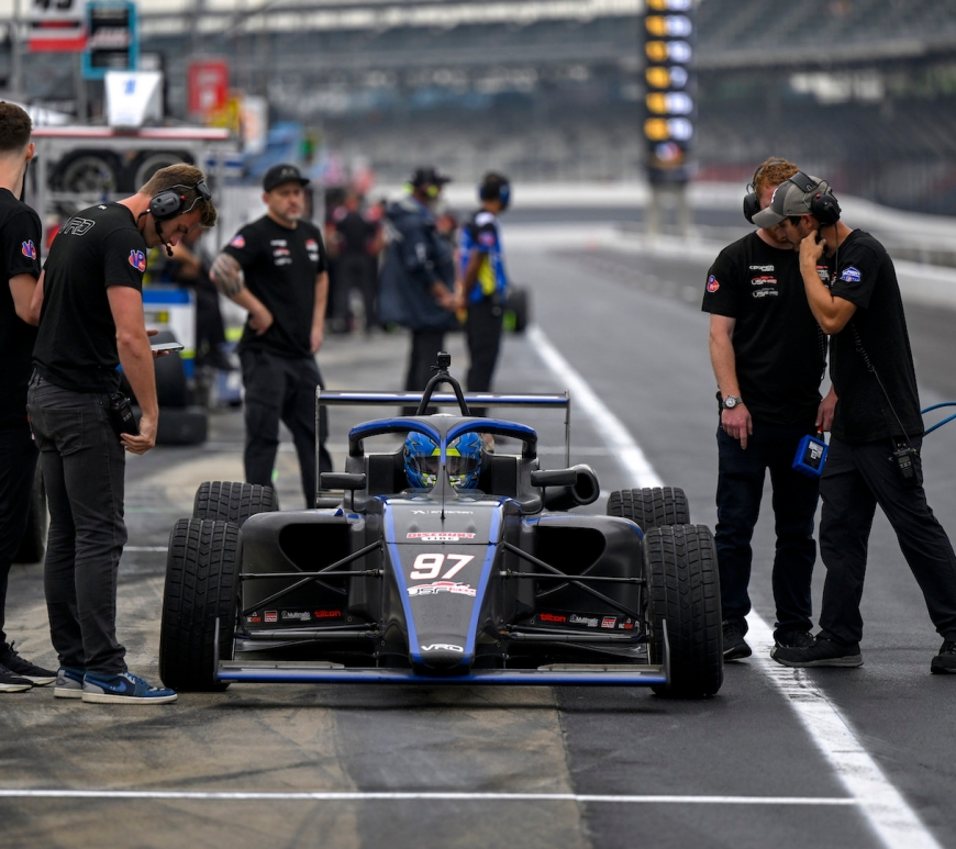 A blue and black car in pit lane with engineers beside and around it