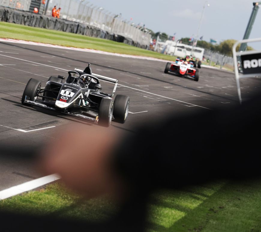A black and white car driving towards pit boards to take the chequered flag